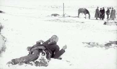 a person lying on the snow with a horse in the background