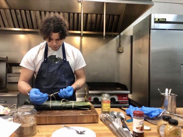 Camren Stotts wraps a whole trout in banana leaves, prepping it to be covered in clay and baked. Courtesy photo.