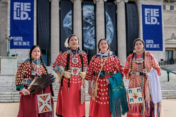 Four women in Apsáalooke attire stand outside the Field Museum in Chicago. These Apsáalooke cultural teachers and others contributed to the exhibition Apsáalooke Women and Warriors. From left to right: Phenocia Bauerle, Charmaine Hill, Nina Sanders, JoRee LaFrance. © Adam Sings In The Timber