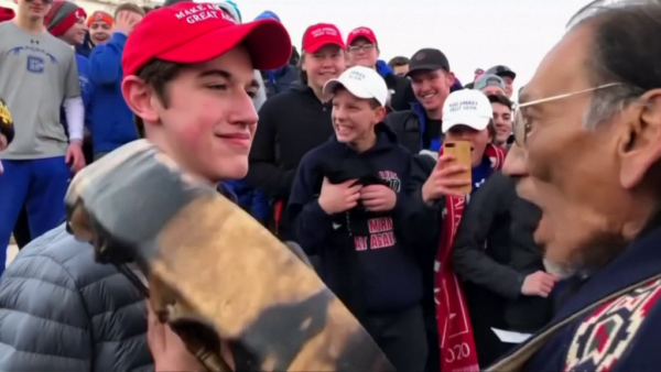 Nathan Phillips (Omaha elder) drumming the AIM anthem as Nicholas Sandmann looks on.