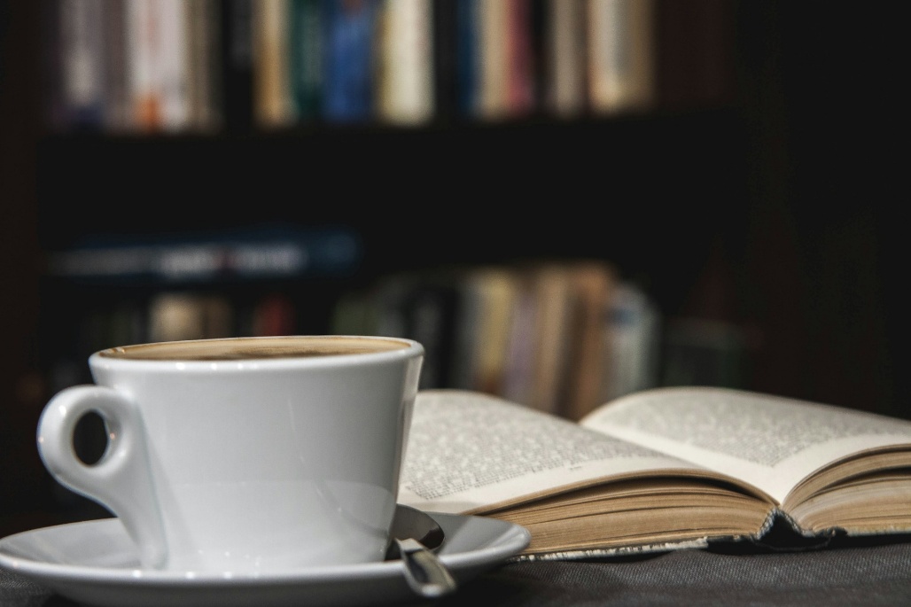 Coffee cup beside an open book in a library setting, representing recommended reading for those asking which books to read to get a comprehensive grasp on tensions between South Korea and Japan.